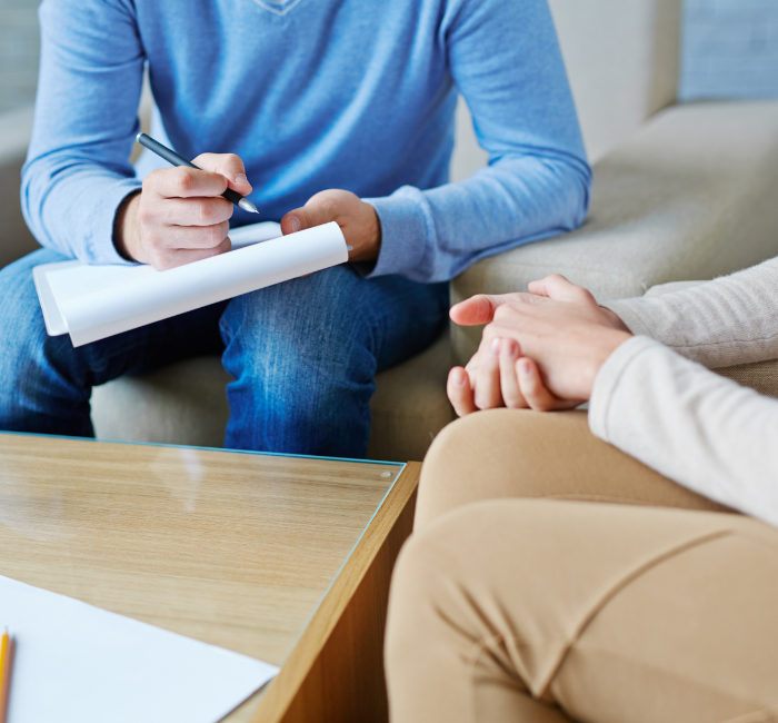 therapy session with close up of clasped hands and a person holding a notepad and writing down notes.