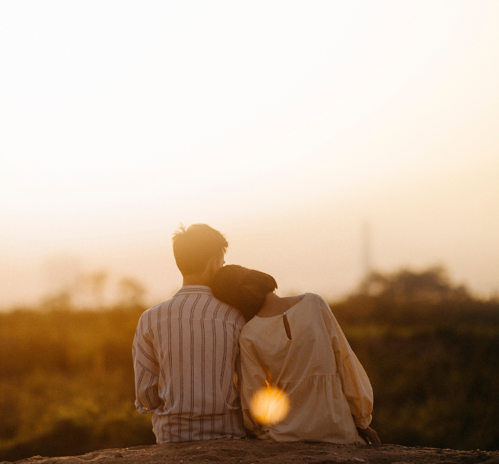 a couple sitting on a log and facing a coastal horizon.