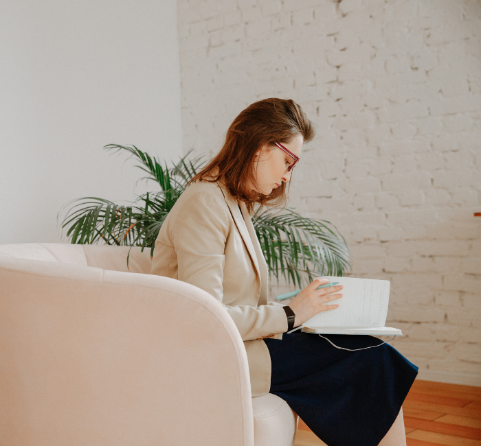 woman sitting on a couch writing in a notebook and taking notes.